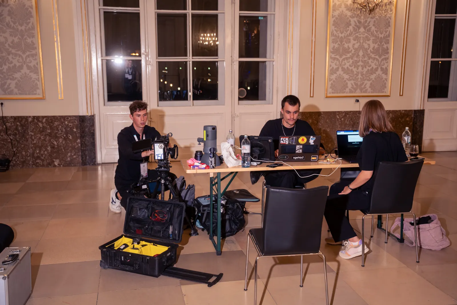 Crew arbeitet nachts an einem Tisch im Saal, Kamerakoffer geöffnet