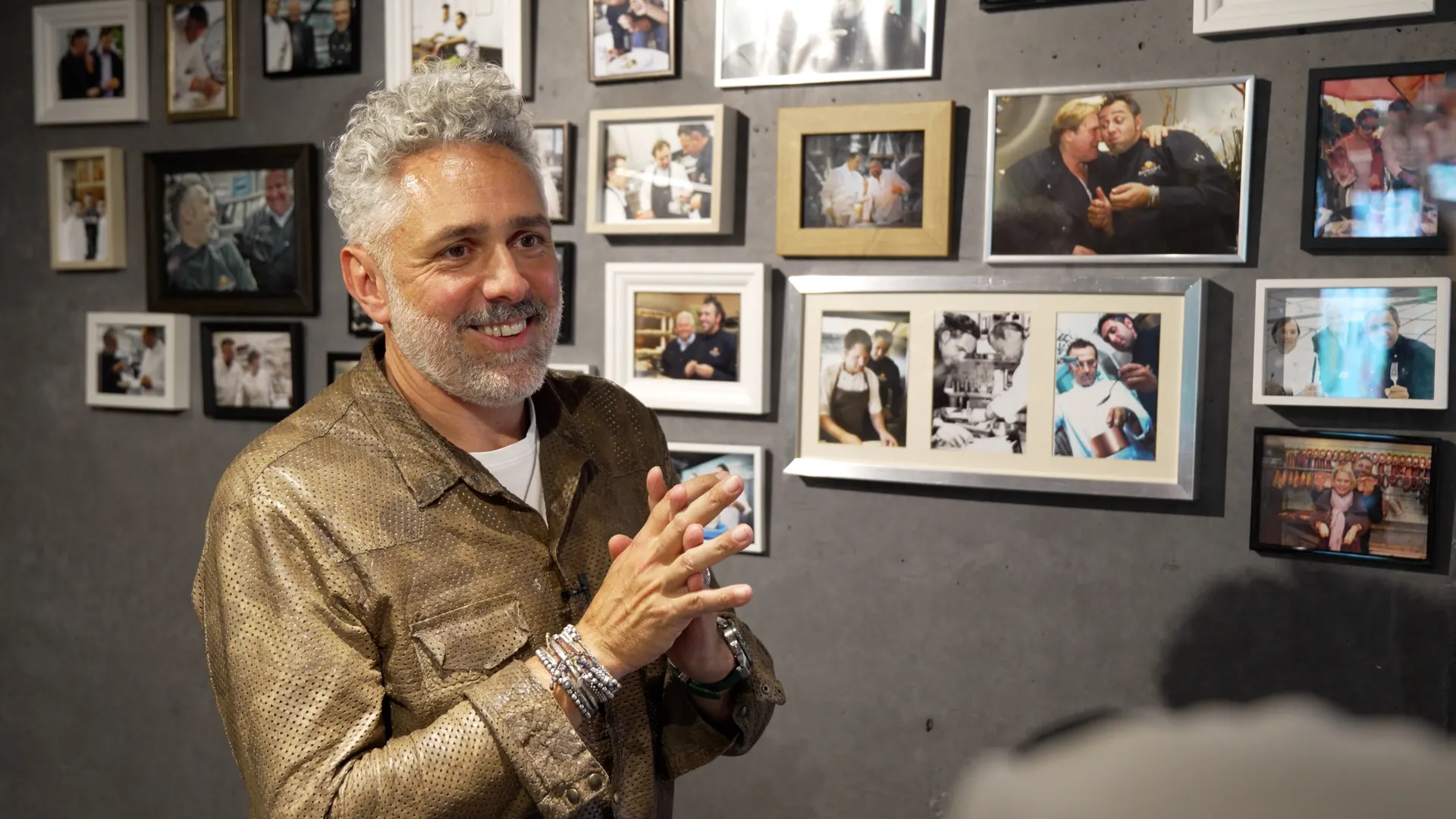 Roland Trettl im Gespräch vor einer Wand mit gerahmten Fotos