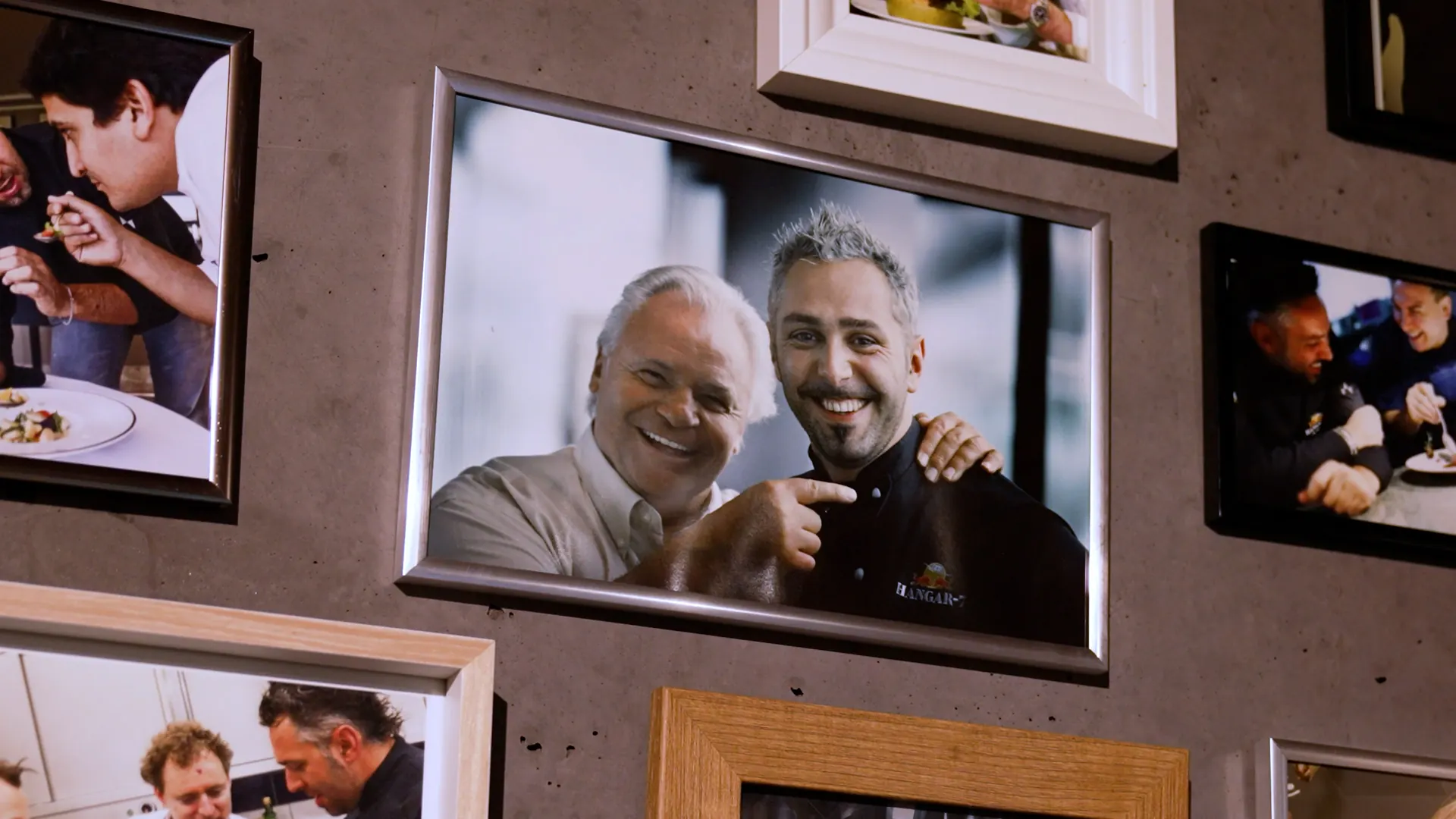Wand mit gerahmten Fotos, im Zentrum zwei Köche